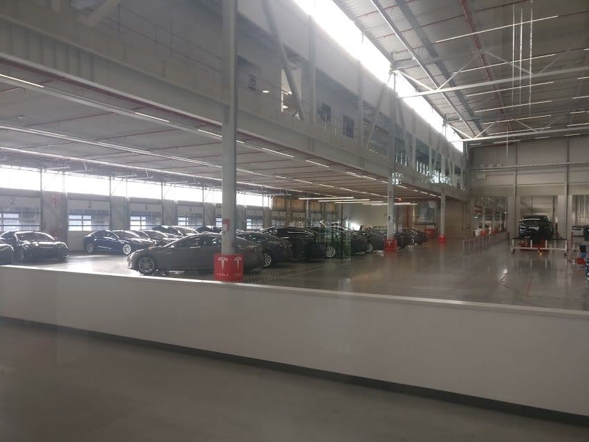Reihe von Tesla Model S in einer hellen Werkshalle in Tilburg, davor rote Tesla-Pylonen