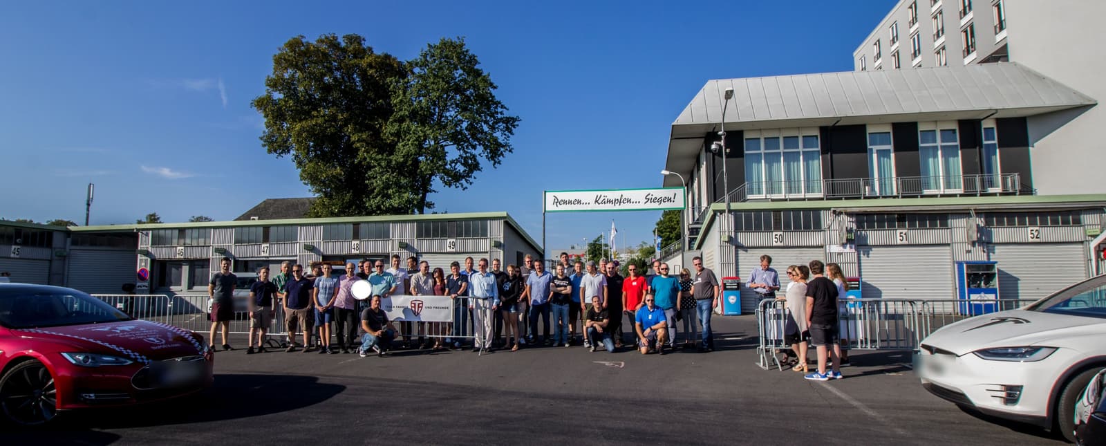 Rund fünfzig Teilnehmende stehen mit dem Vereinsbanner vor den Boxen am Nürburgring