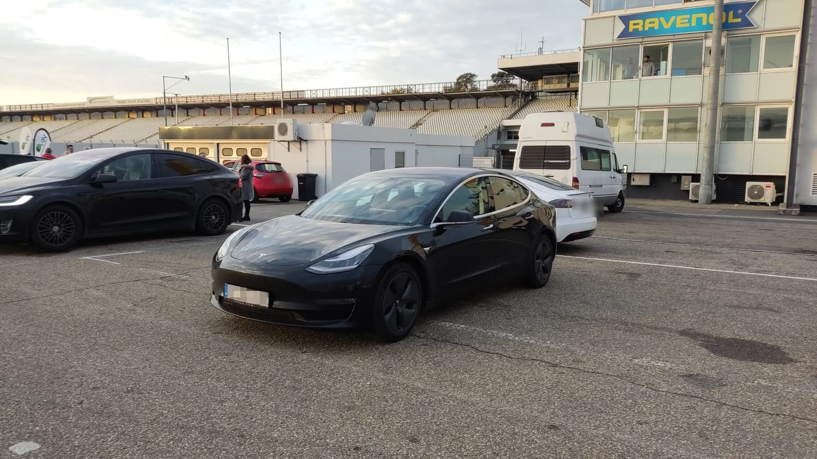 Schwarzer Tesla Model 3 im Fahrerlager des Hockenheimrings, dahinter Tribüne und Zeitnahmeturm