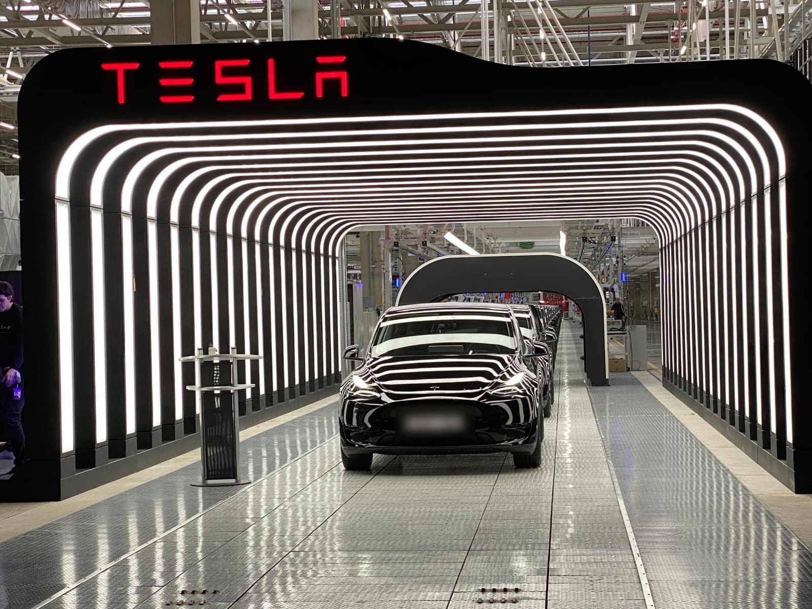 Reihe neuer schwarzer Model Y unter dem beleuchteten Tesla-Bogen in der Werkshalle in Grünheide