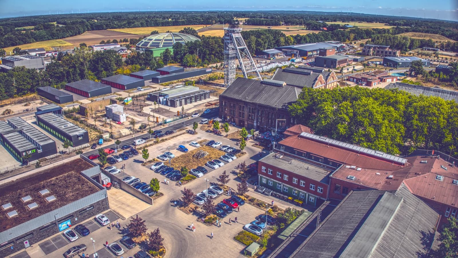 Luftaufnahme des Zechengeländes in Dorsten mit Förderturm, Backsteinhallen und Parkflächen voller Teslas