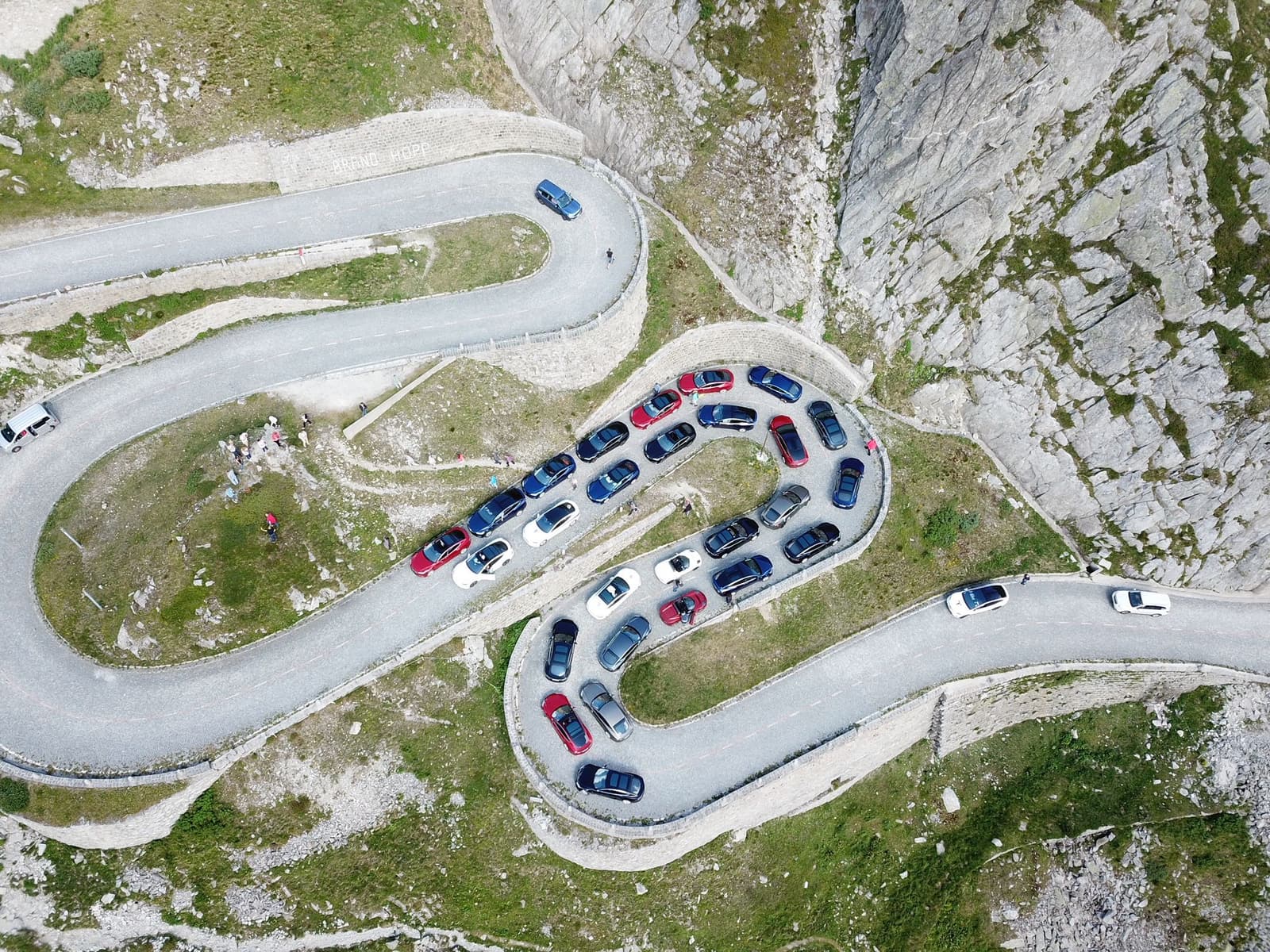 Luftaufnahme der Tremola-Serpentinen am Gotthardpass, in zwei Kehren parkt eine Gruppe Fahrzeuge