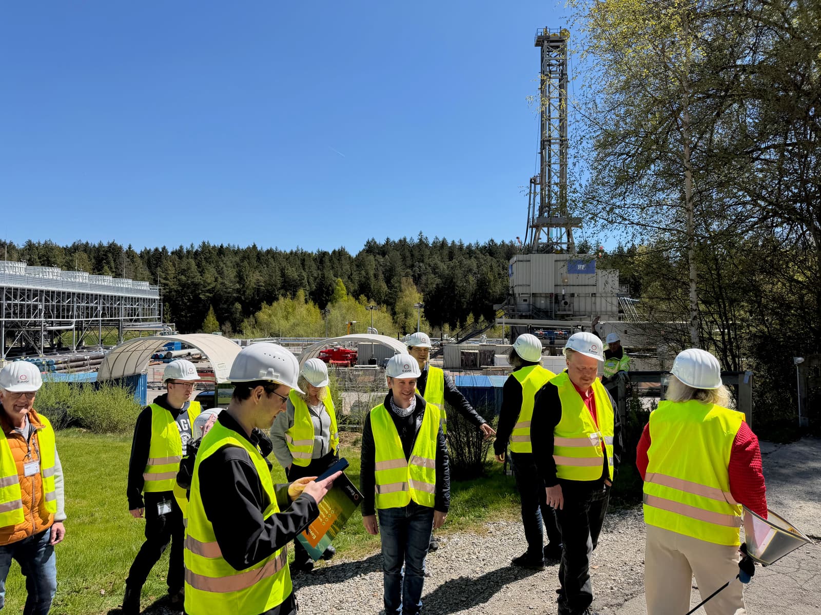 Die Gruppe in Warnwesten und Helmen vor dem Bohrturm des Kraftwerks