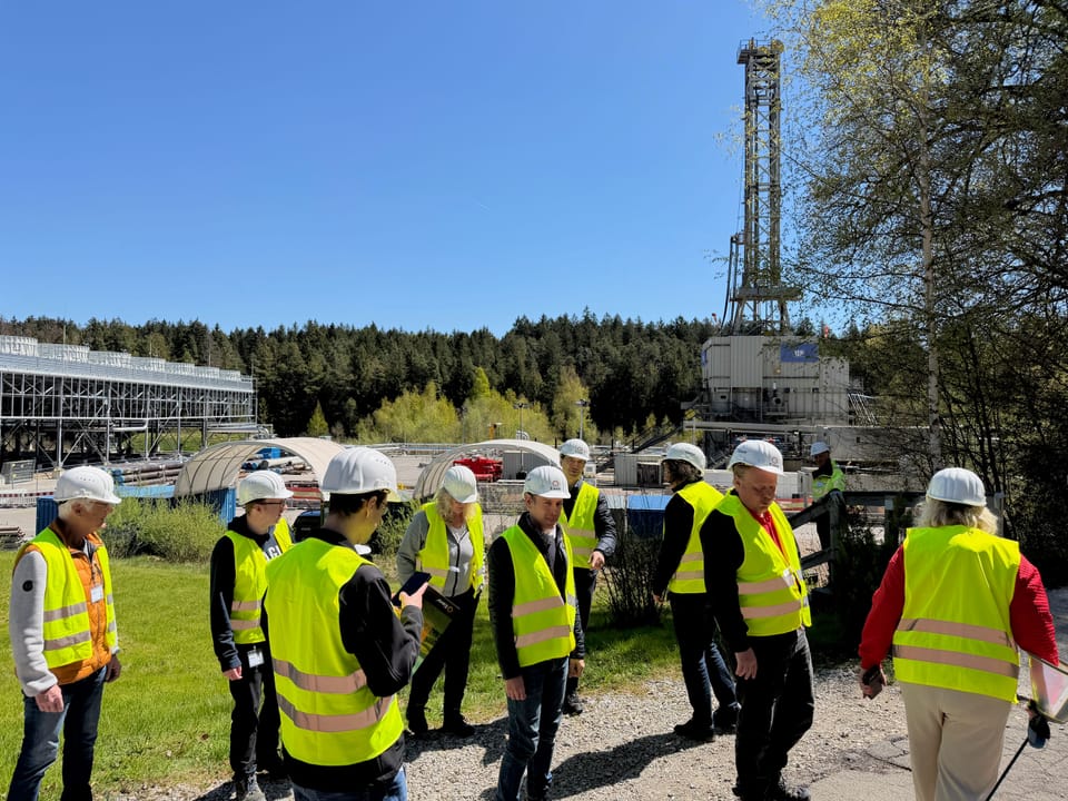 Gruppe in Warnwesten und Helmen vor dem Bohrturm