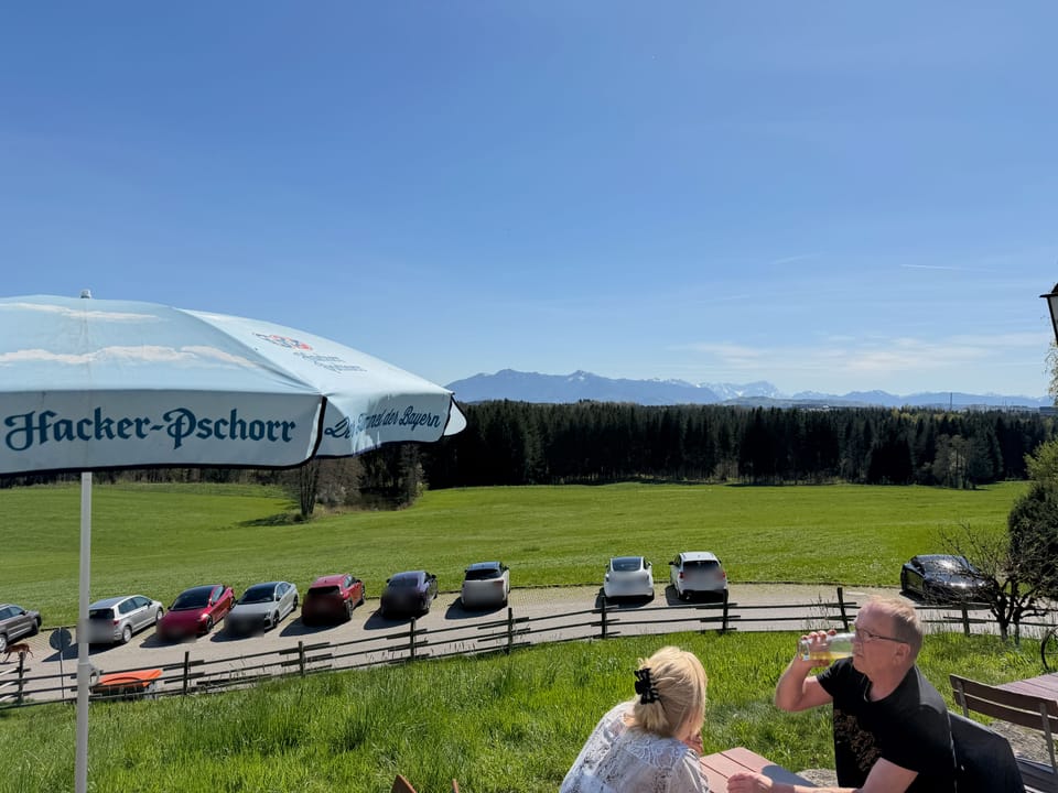 Blick von der Terrasse über die Wiesen zu den Alpen, davor ein Sonnenschirm