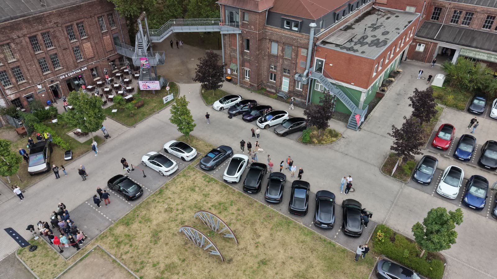 Luftaufnahme des Zechengeländes: Teslas in Reihen zwischen den Backsteingebäuden, dazwischen Besucher