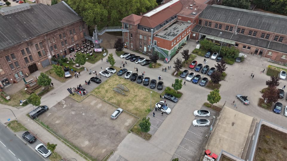 Blick von oben auf den Innenhof mit Fahrzeugen, Bäumen und Besuchern