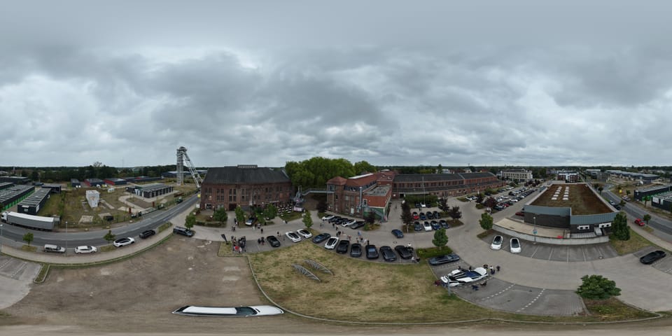Weites Panorama des Zechengeländes aus der Luft, links das Fördergerüst, überall geparkte Fahrzeuge