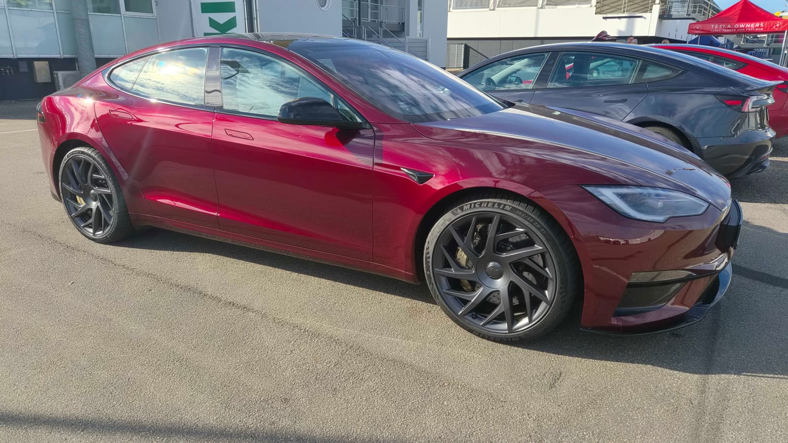 Dunkelrotes Tesla Model S Signature Edition im Fahrerlager des Hockenheimrings, dahinter ein weiterer Tesla und der rote Pavillon des Vereins
