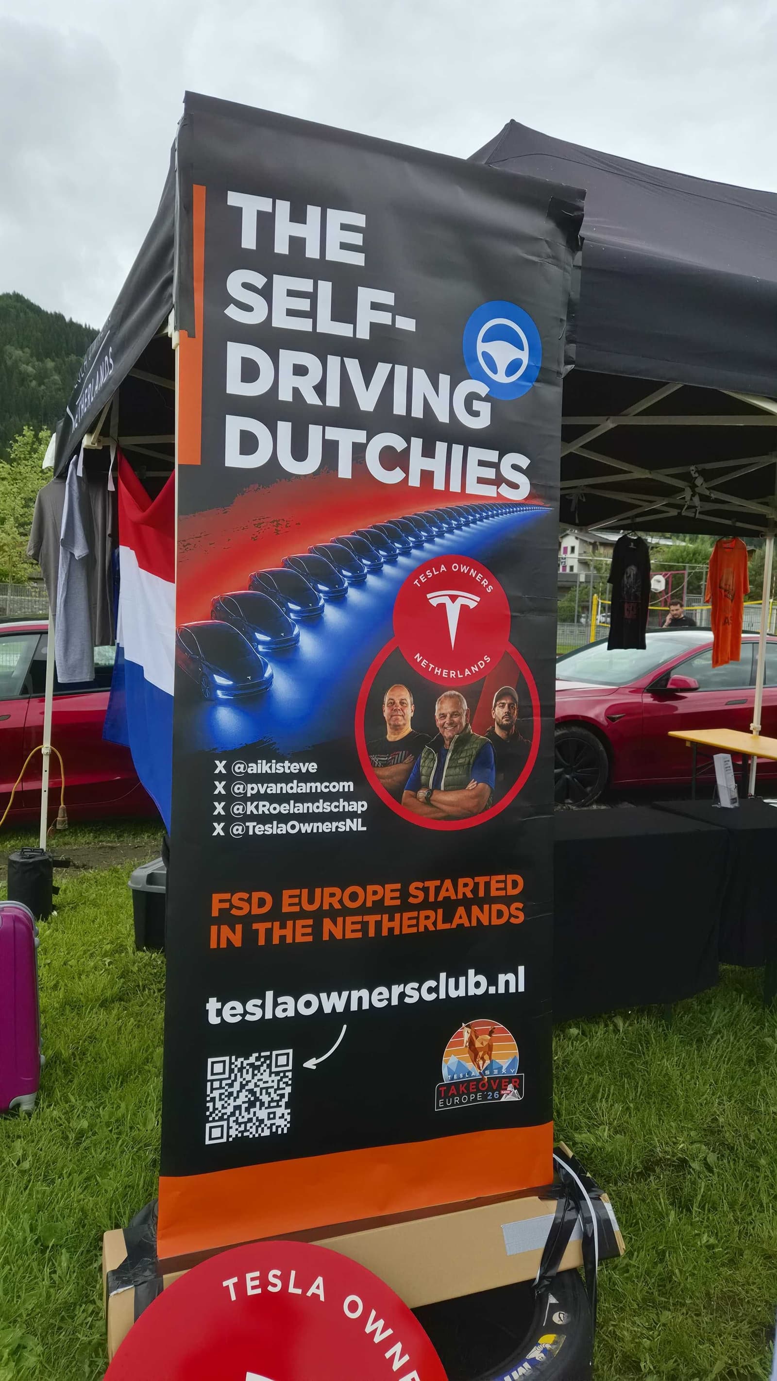 Aufsteller des Tesla Owners Club Netherlands mit niederländischer Flagge daneben, davor der Verkaufstisch des Clubs