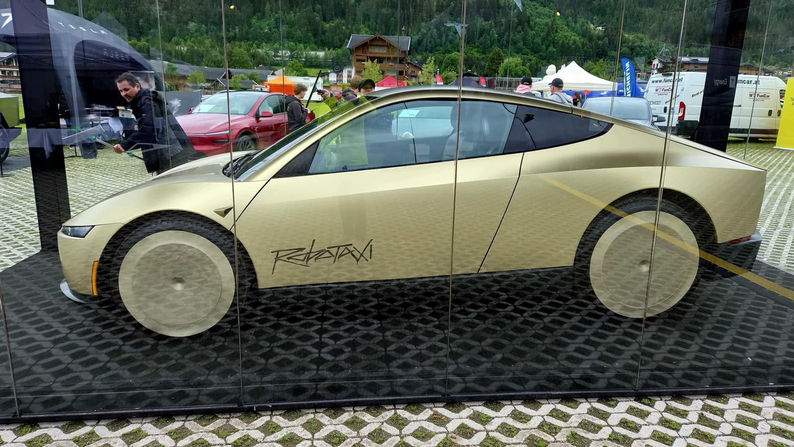 Goldfarbenes Robotaxi hinter Glas auf einem schwarzen Podest, dahinter das Veranstaltungsgelände