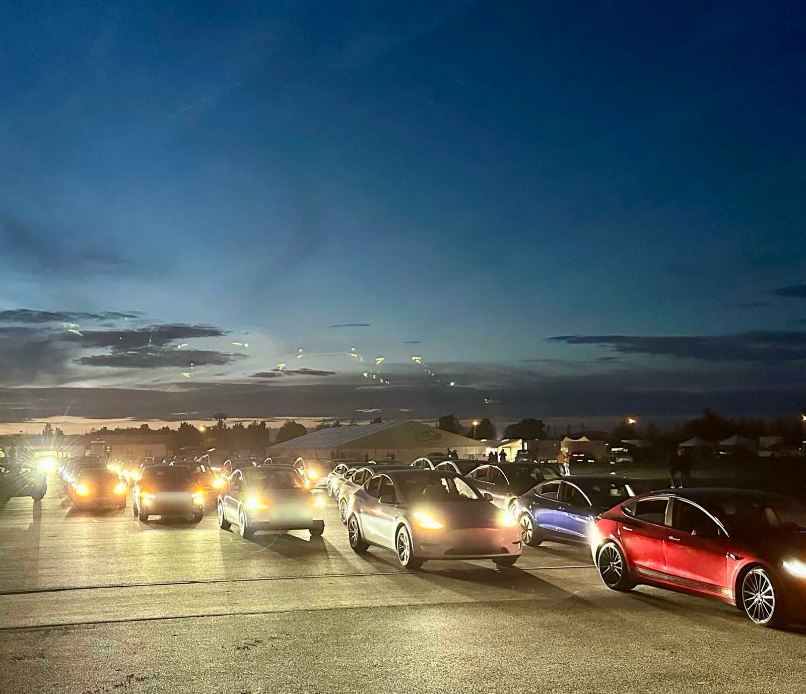 Reihen von Teslas mit eingeschalteten Scheinwerfern in der Abenddämmerung vor der Lightshow