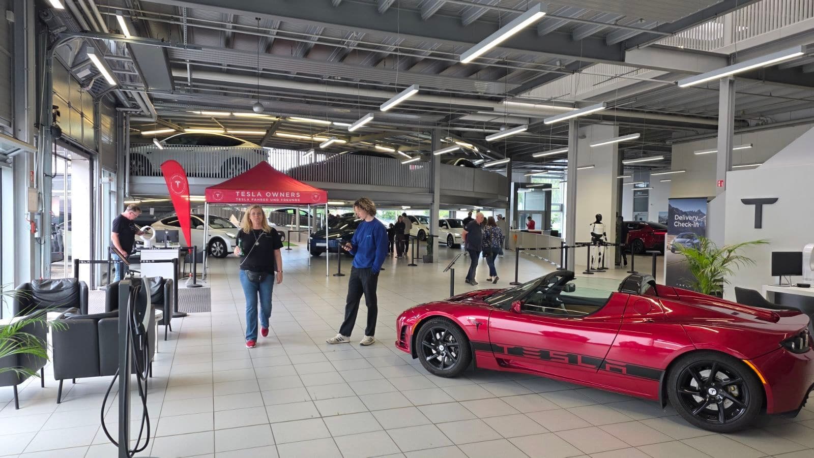 Roter Tesla Roadster von der Seite im Ausstellungsraum, im Hintergrund der Vereinsstand und Besucher