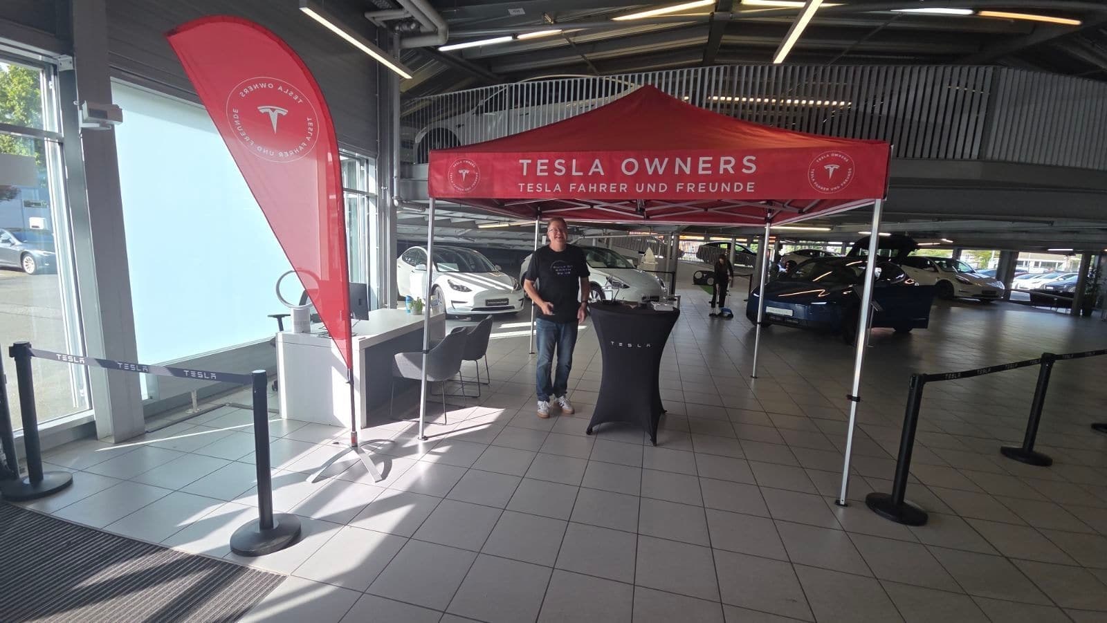 Roter Pavillon mit der Aufschrift Tesla Owners, Tesla Fahrer und Freunde, daneben eine Beachflag im Ausstellungsraum