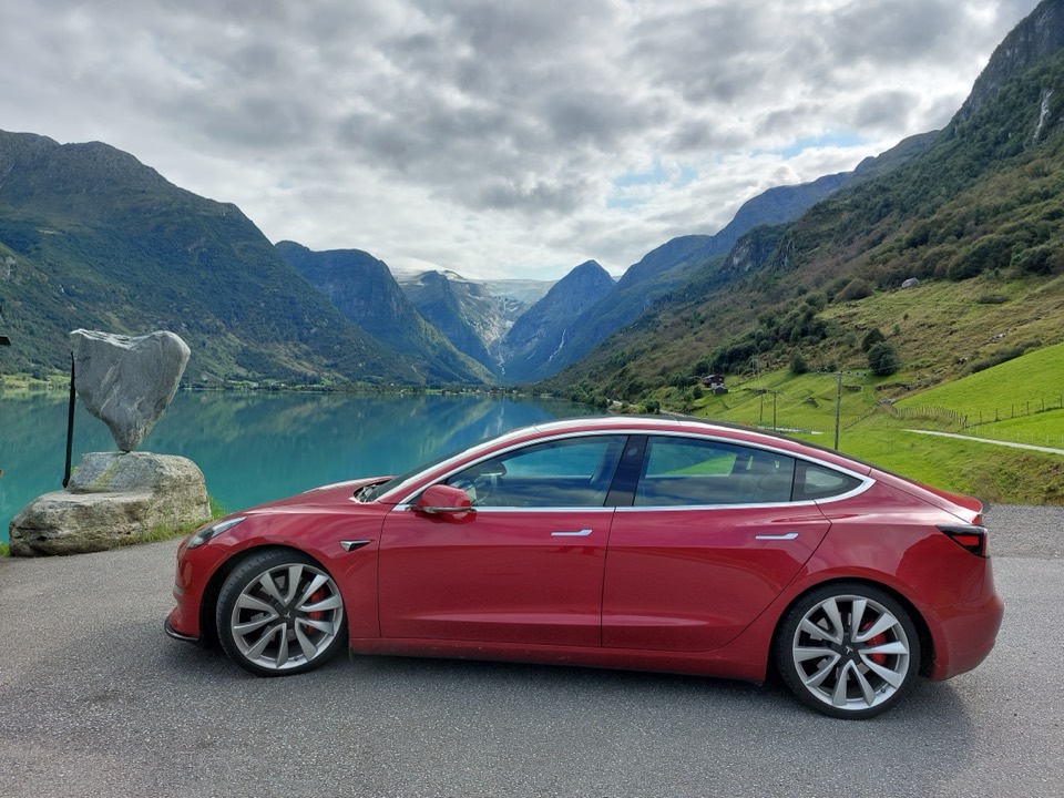 Roter Tesla Model 3 an einem norwegischen Fjord mit Gletscherblick