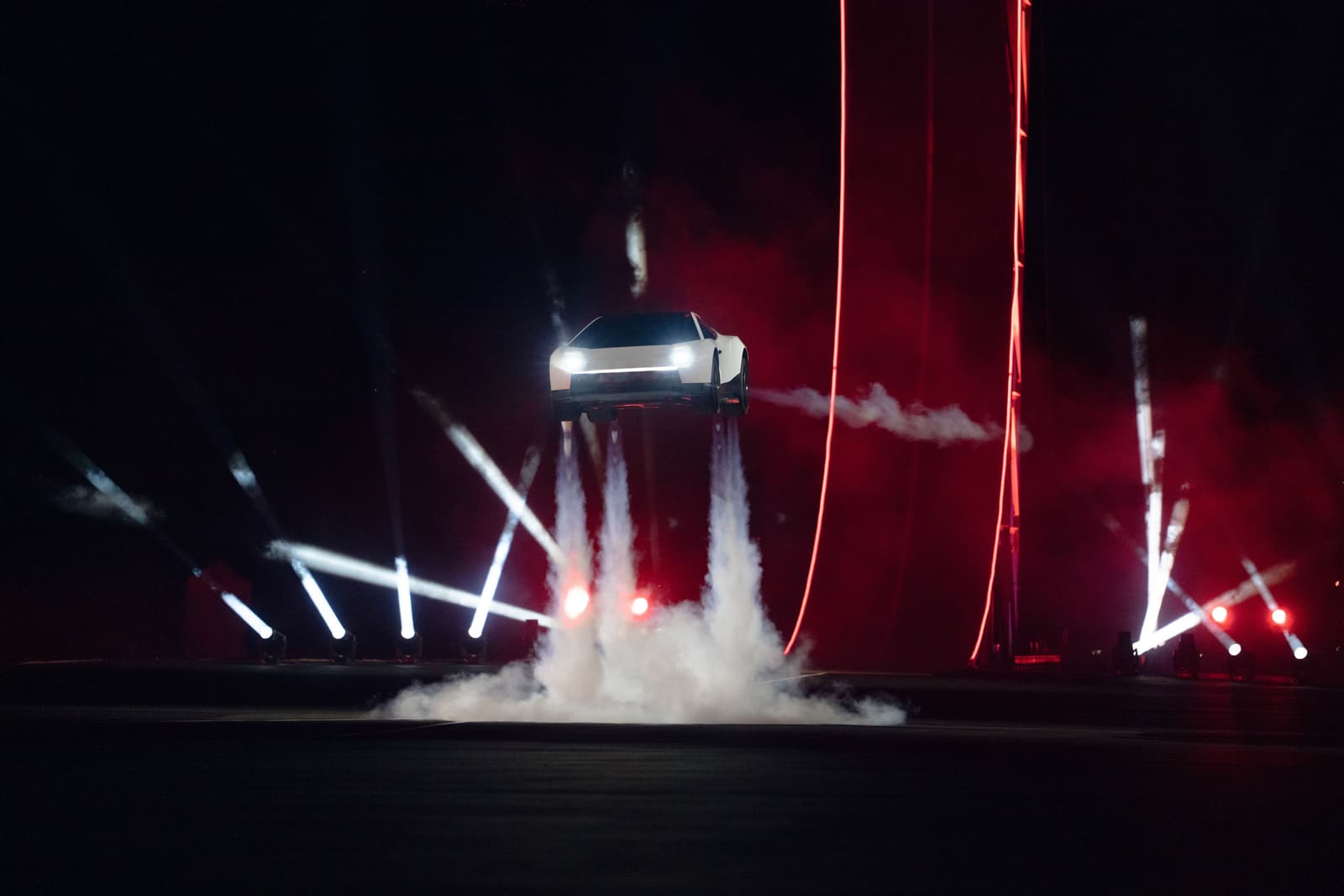 Der Roadster schwebt mit zündenden Triebwerken über dem Boden, Rauch unter dem Wagen, rotes Licht im Hintergrund