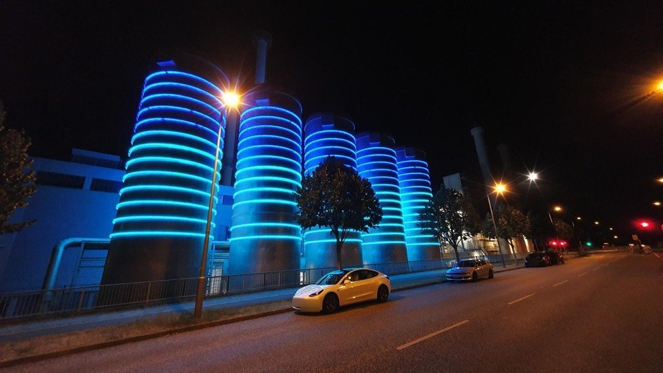 Beleuchtete Industriearchitektur bei Nacht, davor ein Tesla Model Y