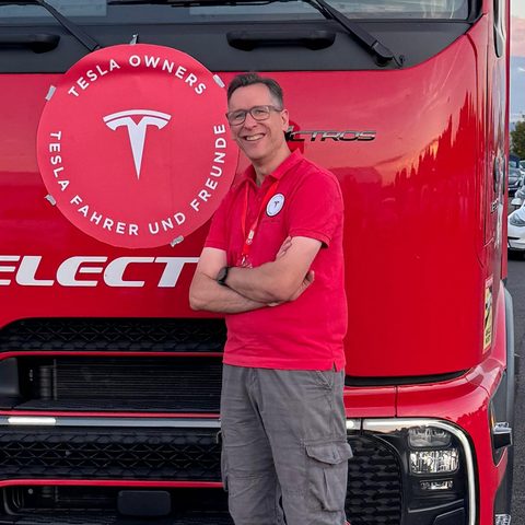 Lars Hendrichs vor einem roten Elektro-Lastwagen, daneben das Vereinslogo